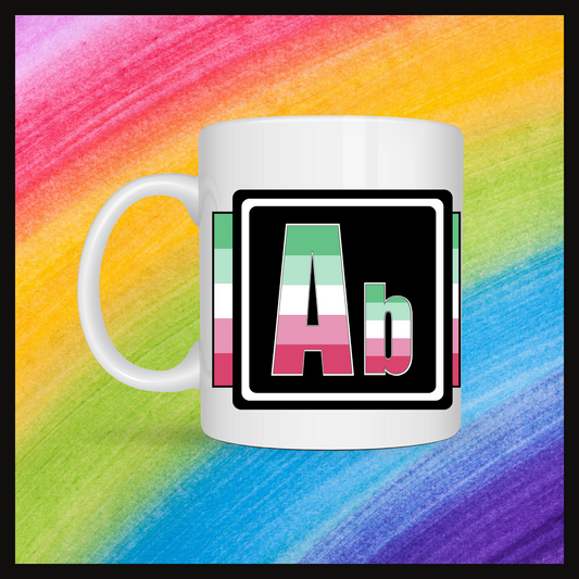 White mug with a 3 inch square containing the element’s symbol (Ab). Symbol is made with the colors of that element’s flag on a black background. The pride flag is displayed behind the symbol. Behind the mug is a rainbow background.