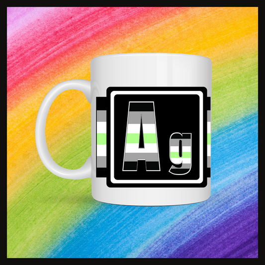 White mug with a 3 inch square containing the element’s symbol (Ag). Symbol is made with the colors of that element’s flag on a black background.The pride flag is displayed behind the symbol.