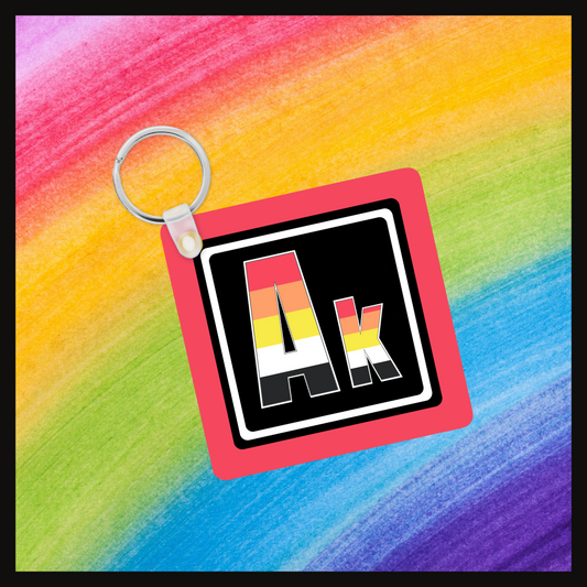 Keychain with the Element symbol (Ak) with a design based on the colors of that element’s flag in a black square with a red background. Behind the keychain is a rainbow background.