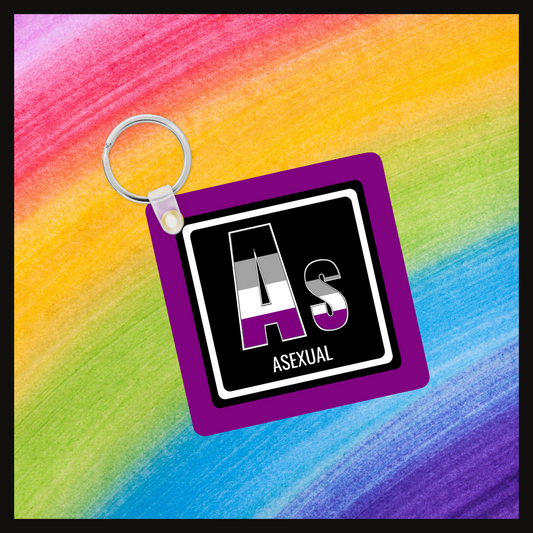 Keychain with the element symbol (As) and name (Asexual) with a design based on the colors of that element’s flag in a black square with a purple background. Behind the keychain is a rainbow background.