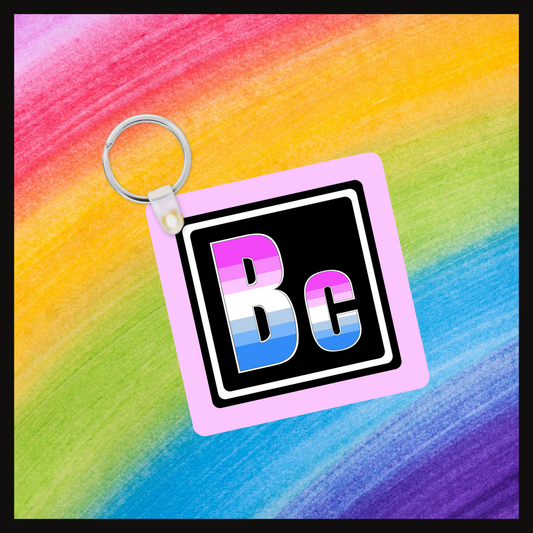 Keychain with the element symbol (BC) with a design based on the colors of that element’s flag in a black square with a pink background. Behind the keychain is a rainbow background.