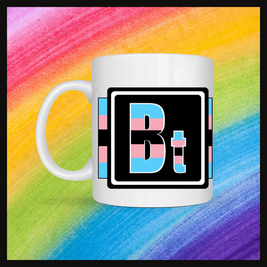 White mug with a 3 inch square containing the element’s symbol (Bt). Symbol is made with the colors of that element’s flag on a black background. Behind the mug is a rainbow background.
