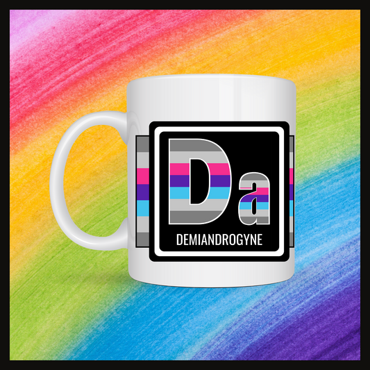 White mug with a 3 inch square containing the element’s symbol (Da) and name (Demiandrogyne). Symbol is made with the colors of that element’s flag in a black square with the element’s flag behind the square. Behind the mug is a rainbow background.