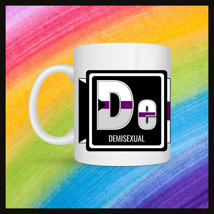 White mug with a 3 inch square containing the element’s symbol (De) and name (Demisexual). Symbol is made with the colors of that element’s flag in a black square with the element’s flag behind the square. Behind the mug is a rainbow background.