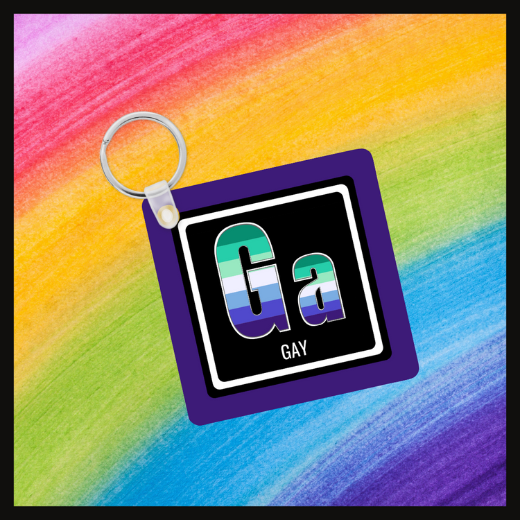 Keychain with the element symbol (Ga) and name (gay) with a design based on the colors of that element’s flag in a black square with a purple background. Behind the keychain is a rainbow background.