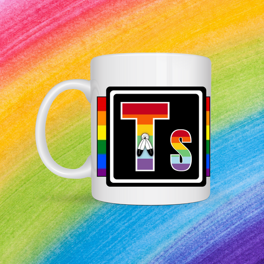 White mug with a 3 inch square containing the element’s symbol (Ts). Symbol is made with the colors of that element’s flag in a black square with the element’s flag behind the square. Behind the mug is a rainbow background.
