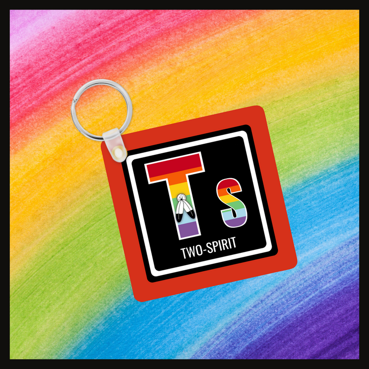 Keychain with the element symbol (Tw) and name (Two-Spirit) with a design based on the colors of that element’s flag in a black square with a red background. Behind the keychain is a rainbow background.