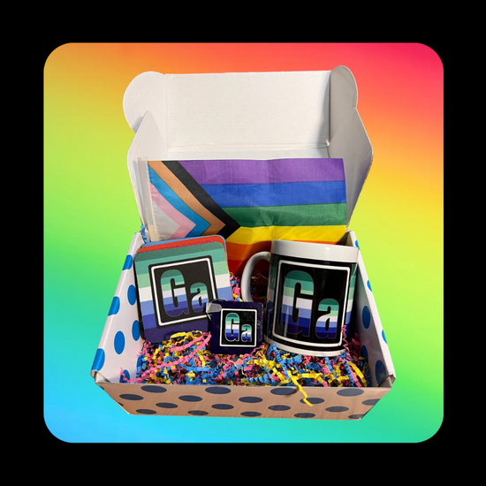 This is our Gay Element Gift Box - on a rainbow background inside a dotted blue box that holds a Queer Element Mug, Keychain and a set of our LGBTQ Coasters