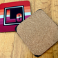 The Lesbian Element coaster. On the left is the front of the Lesbian element with the colors of the lesbian flag. On the right is te back of our coasters, which have cork across the back of the coaster. 