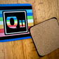 The Queer Element coaster. On the left is the front of the Queer element with the colors of the Queer flag. On the right is te back of our coasters, which have cork across the back of the coaster. 
