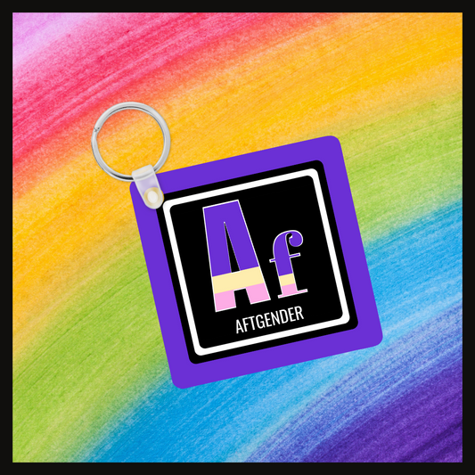 Keychain with the  element symbol (Af) and name (Aftgender) with a design based on the colors of that element’s flag in a black square with a purple background. Behind the keychain is a rainbow background.