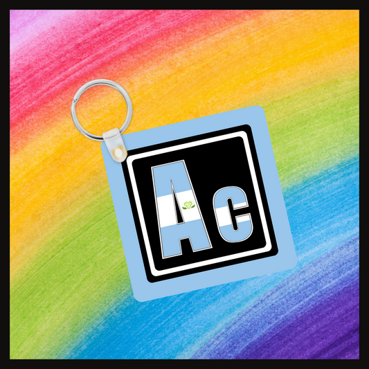 Keychain with the element symbol (Ac) with a design based on the colors of that element’s flag in a black square with a blue background. Behind the keychain is a rainbow background.