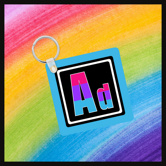Keychain with the element symbol (Ad) with a design based on the colors of that element’s flag in a black square with a blue background. Behind the keychain is a rainbow background.
