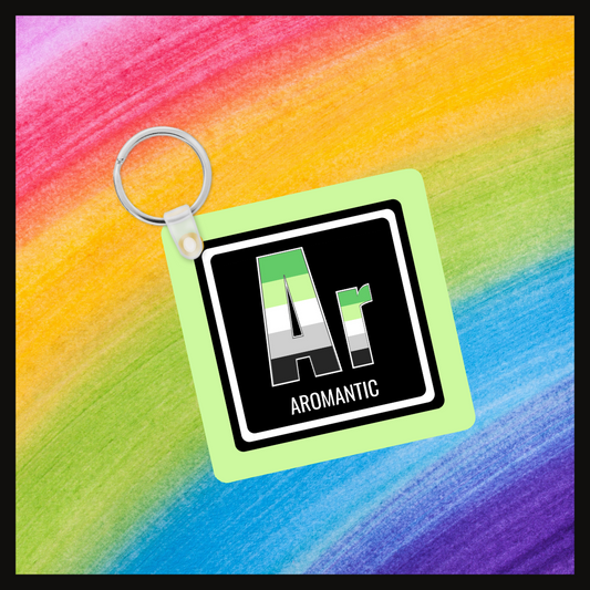 Keychain with the element symbol (Ar) and name (Aromantic) with a design based on the colors of that element’s flag in a black square with a green background. Behind the keychain is a rainbow background.