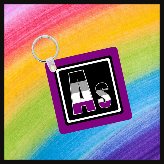 Keychain with the element symbol (As) with a design based on the colors of that element’s flag in a black square with a purple background. Behind the keychain is a rainbow background.