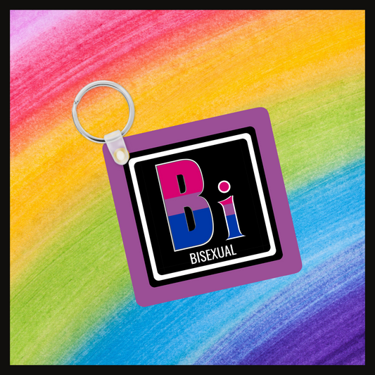 Keychain with the element symbol (Bi) and name (Bisexual) with a design based on the colors of that element’s flag in a black square with a purple background. Behind the keychain is a rainbow background.