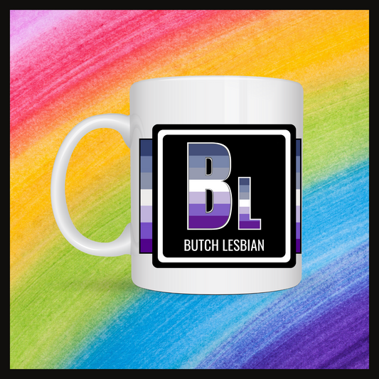 White mug with a 3 inch square containing the element’s symbol (Bl) and name (Butch lesbian). Symbol is made with the colors of that element’s flag in a black square with the element’s flag behind the square. Behind the mug is a rainbow background.