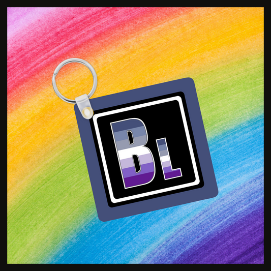 Keychain with the element symbol (Bl) with a design based on the colors of that element’s flag in a black square with a blue background. Behind the keychain is a rainbow background.