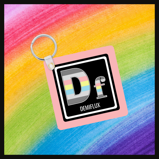 Keychain with the element symbol (Df) and name (demiflux) with a design based on the colors of that element’s flag in a black square with a pink background. Behind the keychain is a rainbow background.