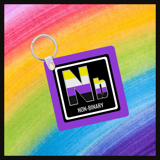 Keychain with the element symbol (Nb) and name (Non-binary) with a design based on the colors of that element’s flag in a black square with a purple background. Behind the keychain is a rainbow background.