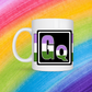 White mug with a 3 inch square containing the element’s symbol (Gq). ymbol is made with the colors of that element’s flag in a black square with the element’s flag behind the square. Behind the mug is a rainbow background.